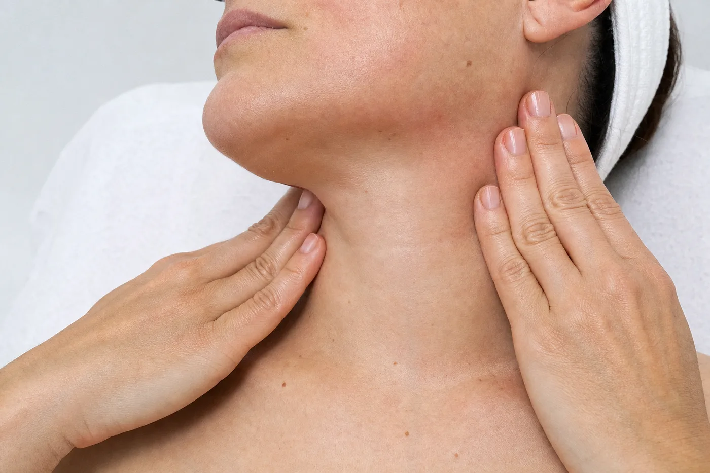 Deux mains remontant le long d’une mâchoire et d’un cou, bandeau de coton blanc en bord de cadre.